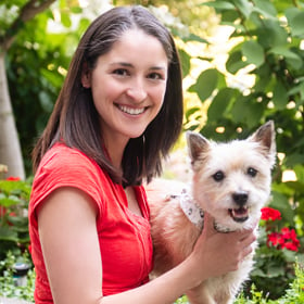 femme portant un petit chien brun clair en souriant