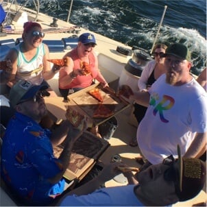 Rover teammates having pizza inside a boat. One is wearing a diversity Rover T-shirt.