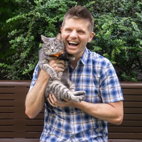 homme portant un chat à rayures grises et blanches en riant